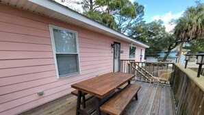 A wooden deck with a picnic table and benches, adjacent to a pink building with windows and a door. - Tybee Pink House (Military & Veteran Discount) (Tybee Island)