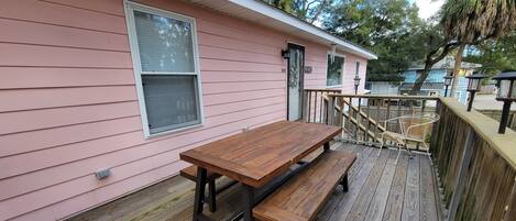 A wooden deck with a picnic table and benches, adjacent to a pink building with windows and a door.