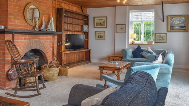 A cozy living room with a brick fireplace, wooden shelves, a television, and a blue sofa. - 5 bedroom accommodation in St Mary&rsquo;s Bay, near Romney Marsh (St Mary&rsquo;s Bay, near Romney Marsh)