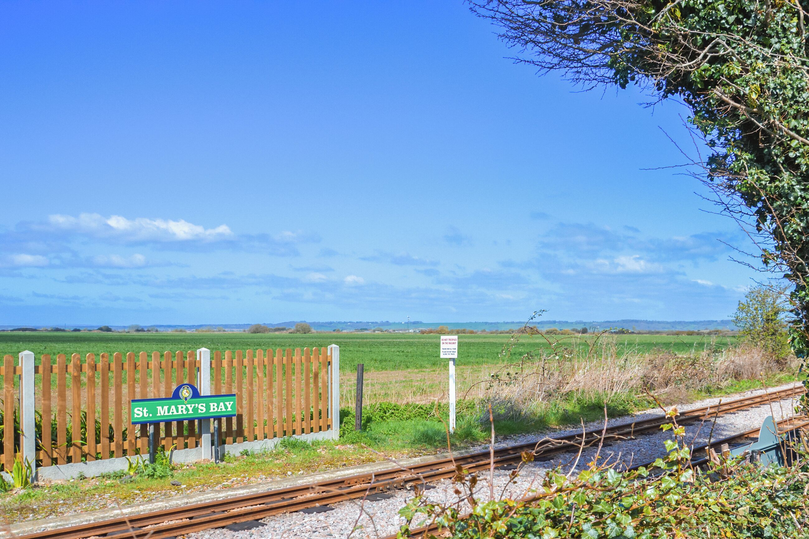 Un paysage rural avec une clôture en bois, une voie ferrée et un panneau indiquant « St. Mary’s Bay ».