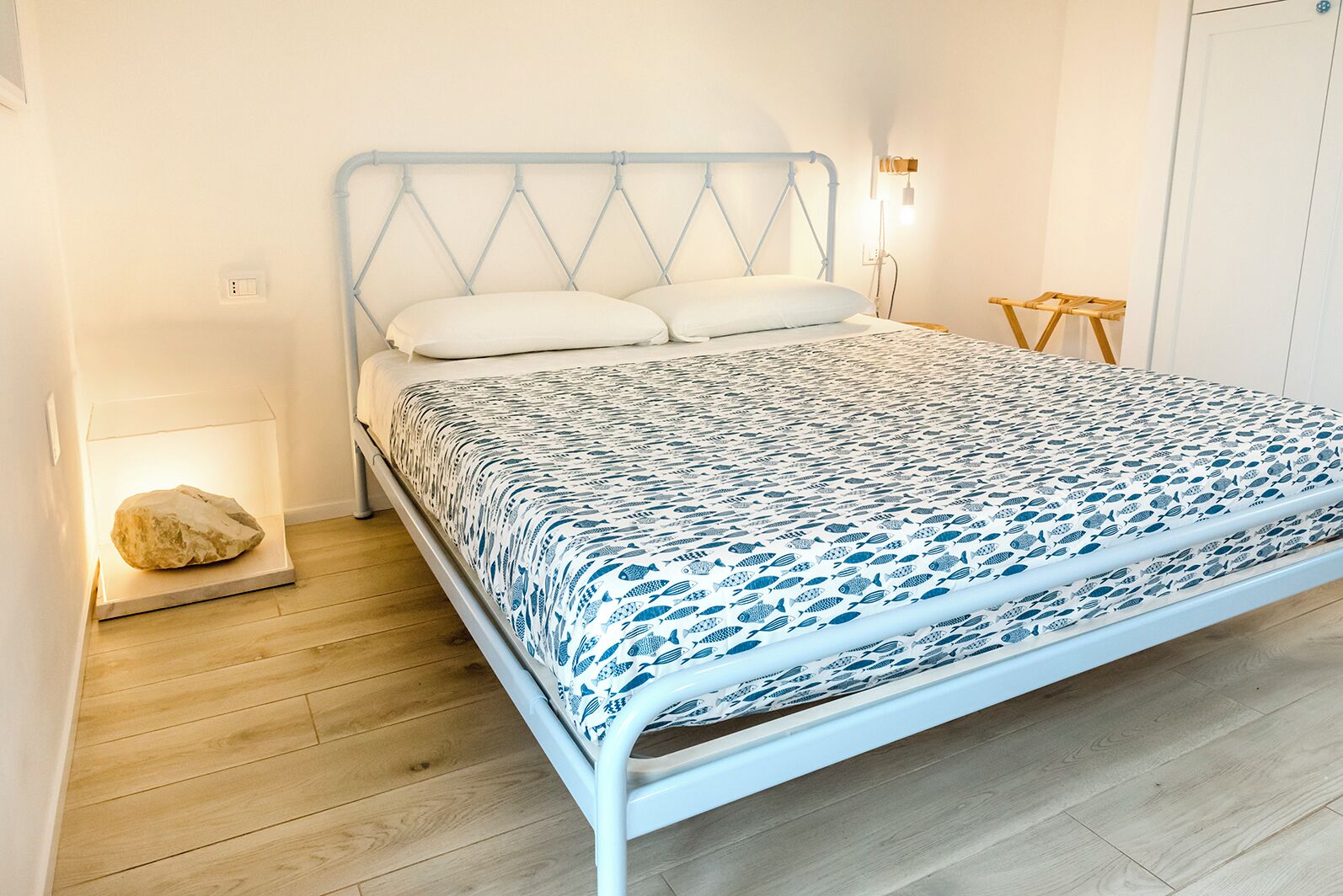 Una cama con estructura metálica blanca, una colcha estampada y dos almohadas.