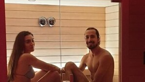 A sauna with two people sitting inside, a wooden bench, and a bucket with a spoon. - Accanto alle Mura Rooms Relax & Spa (Sirolo)