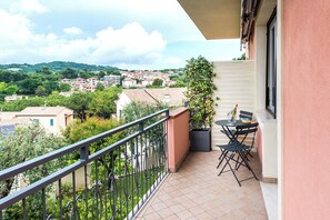 A balcony with a view of a town, a potted plant, and a table with chairs.