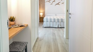 A hallway leading to a bedroom with a bed, a nightstand, a lamp, and a wall with bird decorations. - Accanto alle Mura Rooms Relax & Spa (Sirolo)