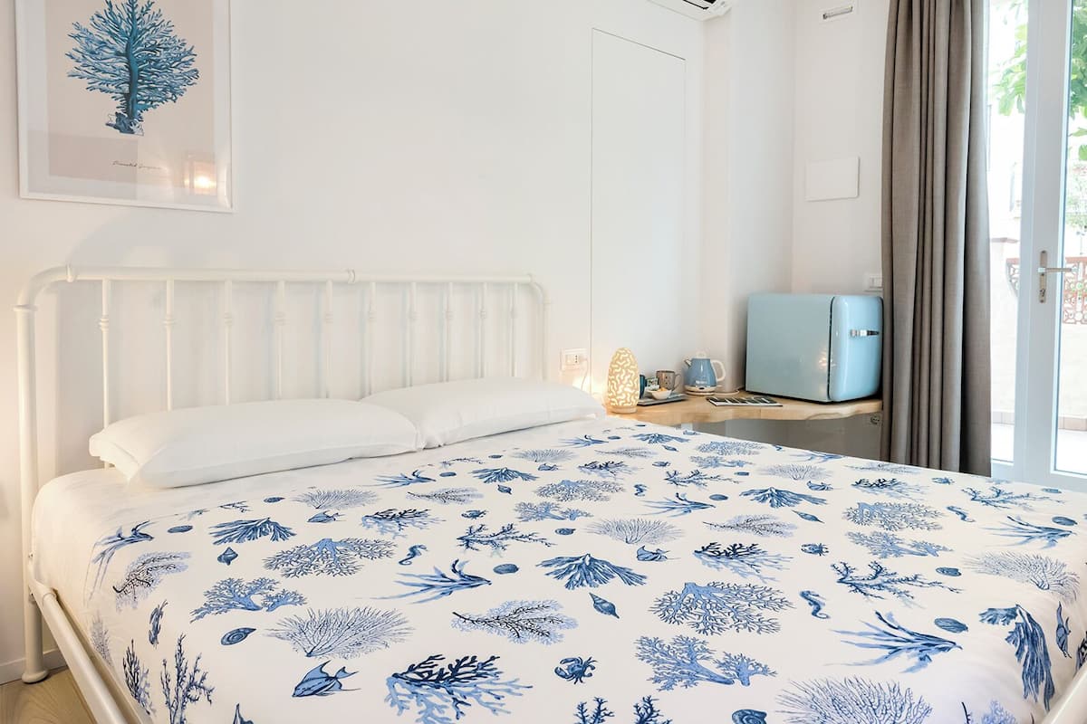 Un dormitorio con cama, una mesita de noche, una maleta azul y un cuadro en la pared.
