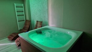 A spa room with a large bathtub, wooden loungers, and a towel rack. - Accanto alle Mura Rooms Relax & Spa (Sirolo)