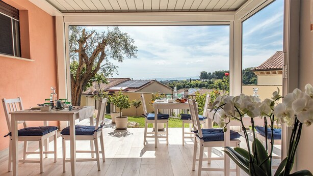 A sunlit patio with a table and chairs, potted plants, and a view of a residential area. - Accanto alle Mura Rooms Relax & Spa (Sirolo)