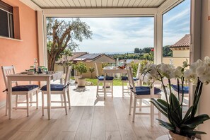 Um pátio ensolarado com mesa e cadeiras, plantas em vasos e vista para uma área residencial.