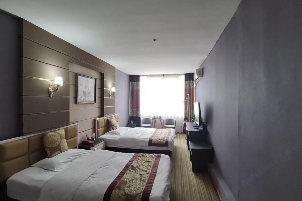 A hotel room with two beds, a desk, a chair, a TV, and a window with curtains.