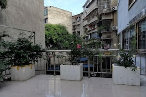 A courtyard with potted plants, a metal gate, and residential buildings in the background.