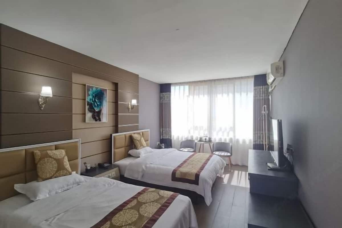 Hotellihuone, jossa on kaksi sänkyä, televisio, työpöytä ja ikkuna, jossa on verhot.