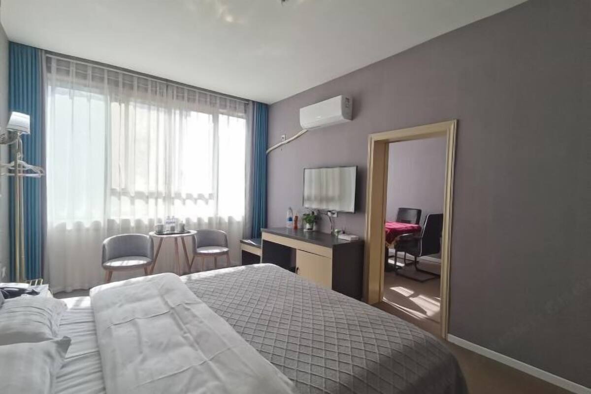 Hotellihuone, jossa on sänky, työpöytä, tuoli, televisio ja ikkuna, jossa on verhot.