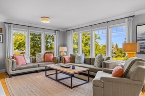 A spacious living room with large windows, a sofa set, a coffee table, and a lamp.