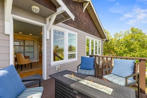 A deck with outdoor furniture, a fire feature, and a view of the interior.