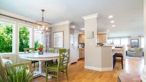 A spacious kitchen with wooden cabinets, a dining area with a round table and chairs, and a view of greenery outside. - Salish Coast Retreat a High End Home with Views (Port Angeles)