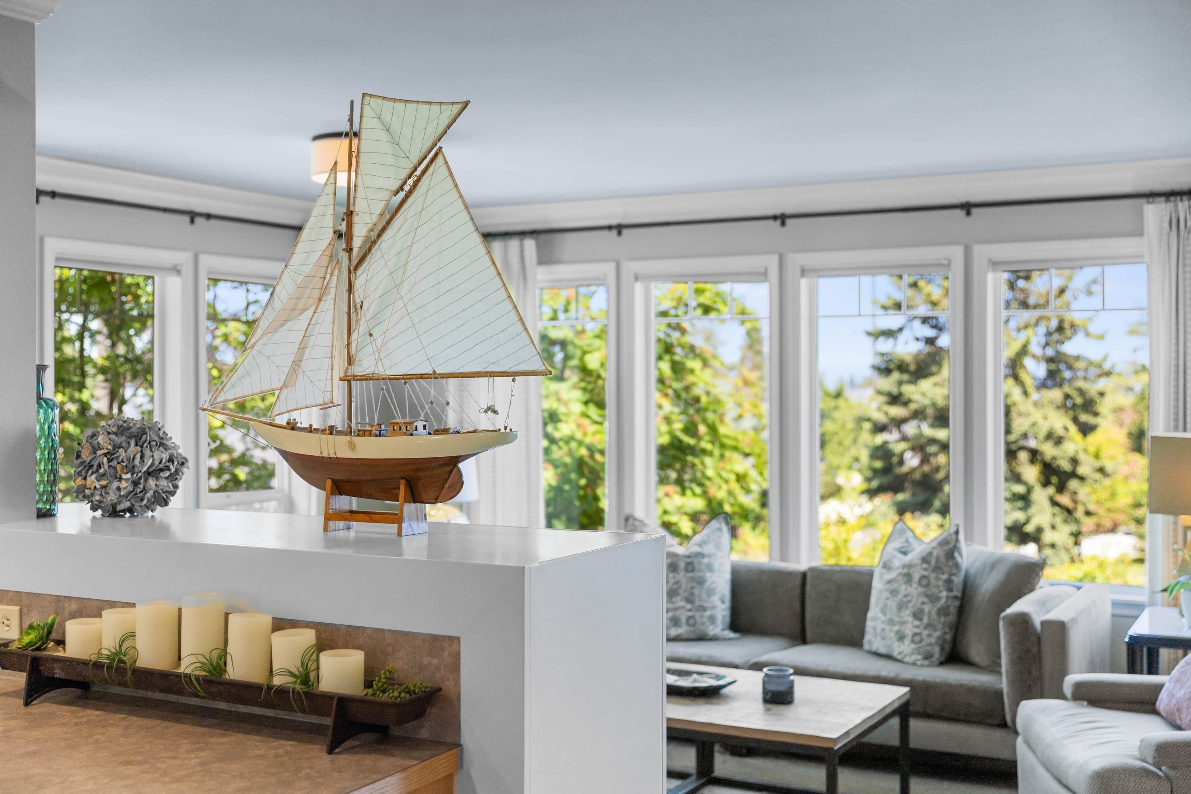 A modern living room with a sailboat model, a sofa, a coffee table, and a shelf with candles.