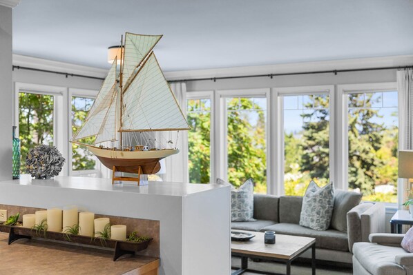 A modern living room with a sailboat model, a sofa, a coffee table, and a shelf with candles.
