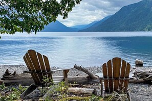 Two Adirondack chairs facing a calm lake with mountains in the background.