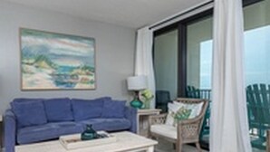 A living room with a blue sofa, a coffee table, a chair, and a painting on the wall. - Island Winds West by Brett/Robinson Vacations (Gulf Shores)