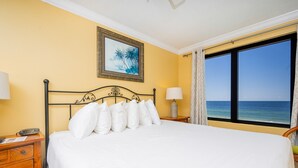 A hotel room with a bed, two bedside tables, a nightstand, a lamp, a framed picture on the wall, and a window with a view of the sea. - Island Winds West by Brett/Robinson Vacations (Gulf Shores)