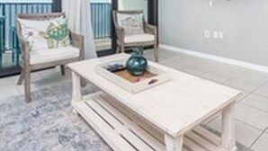 A balcony with two chairs and a table, a TV mounted on the wall, and a view of the sea. - Island Winds West by Brett/Robinson Vacations (Gulf Shores)