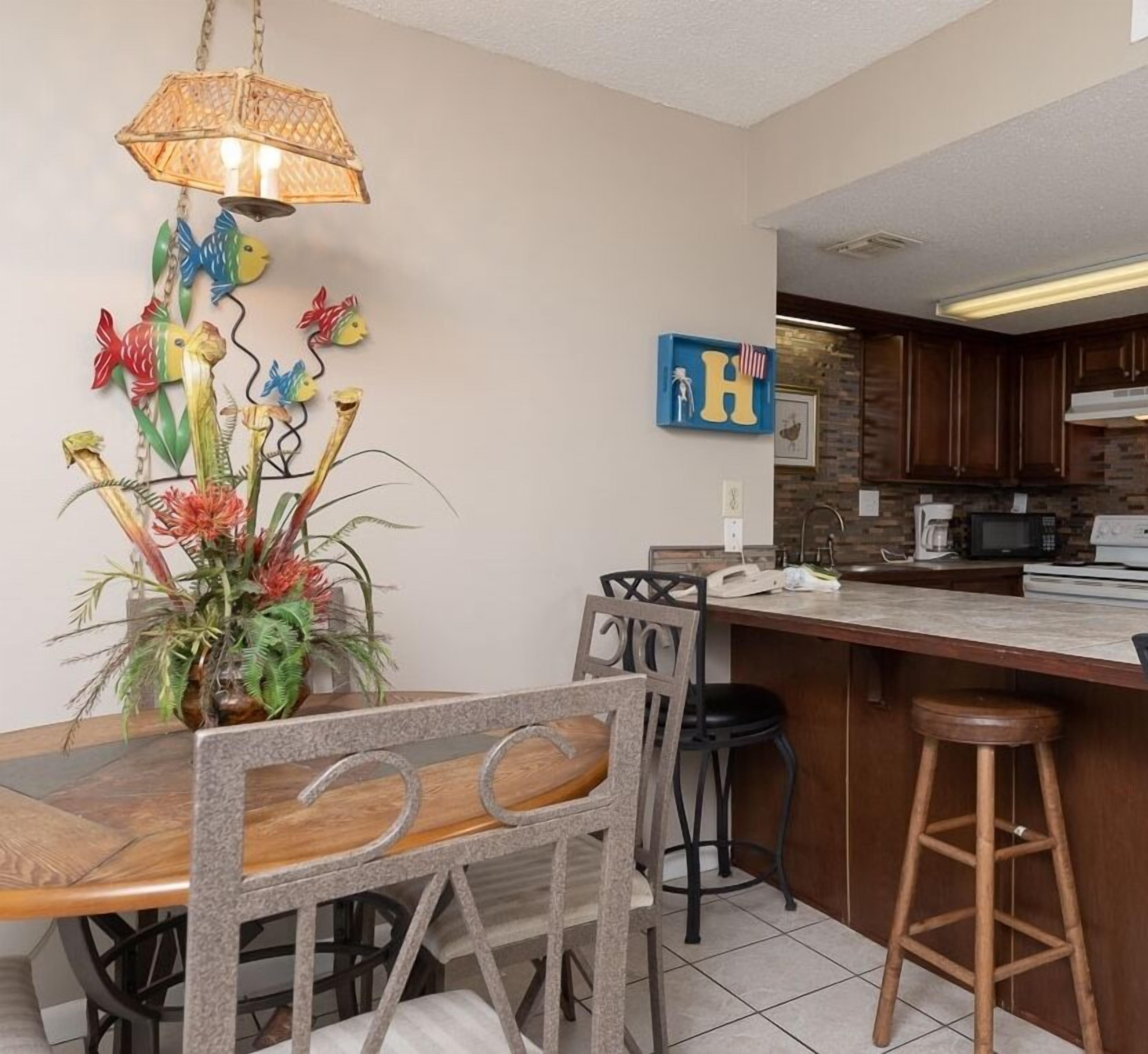 Una cocina moderna con armarios de madera, una isla central y una zona de comedor con mesa y sillas de madera.