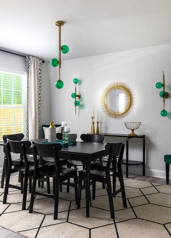 A dining area with a round table, black chairs, a patterned rug, and a decorative mirror with a gold frame.