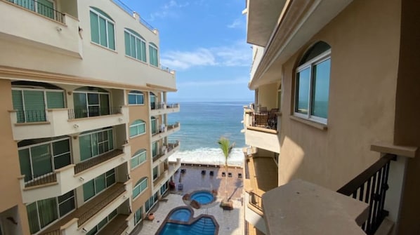 A multi-story hotel with balconies overlooking a pool area and the ocean.