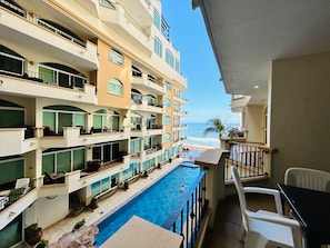A multi-story hotel with balconies, a swimming pool, and a view of the ocean.
