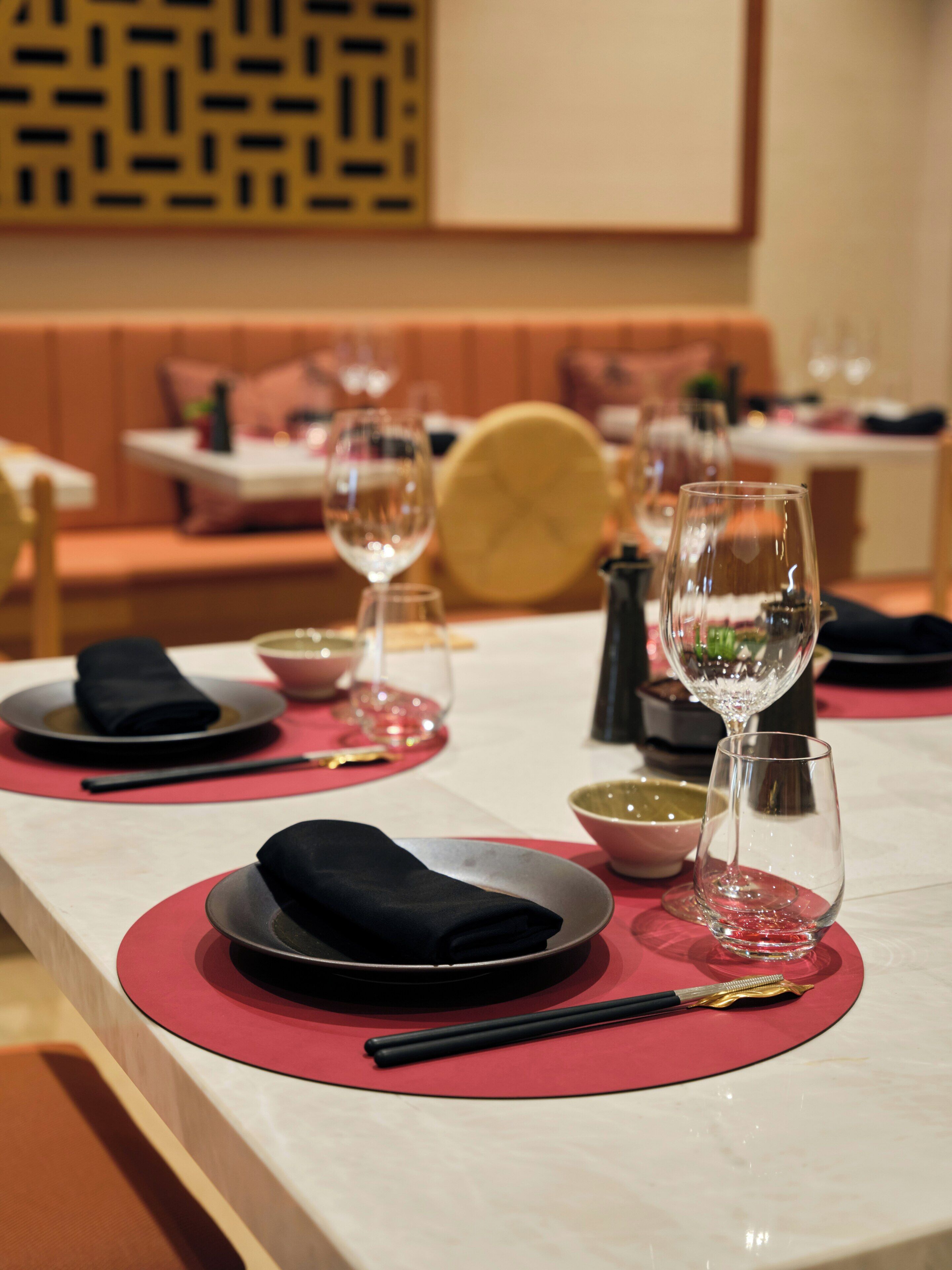 Un ambiente de restaurante con una mesa larga, individuales rojos y copas de cristal.