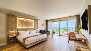 A hotel room with a large bed, a sofa, a dining table, and a balcony with a view. - Hilton Hotel Tahiti (Faaa)
