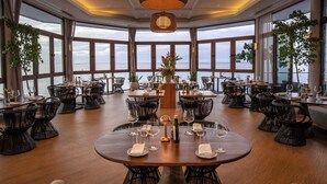 A restaurant with round tables, wicker chairs, and large windows overlooking the sea. - Hilton Hotel Tahiti (Faaa)
