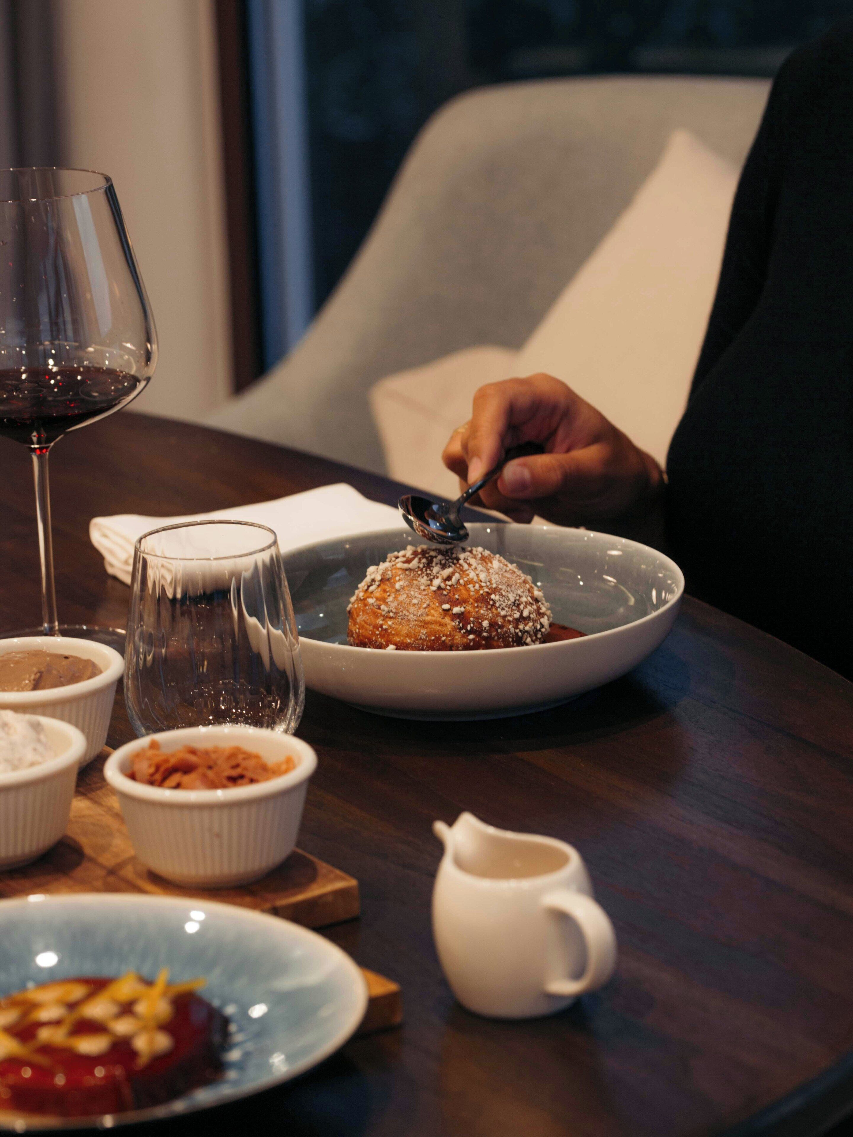 A dining table with a dessert, a glass of red wine, and small bowls of condiments.