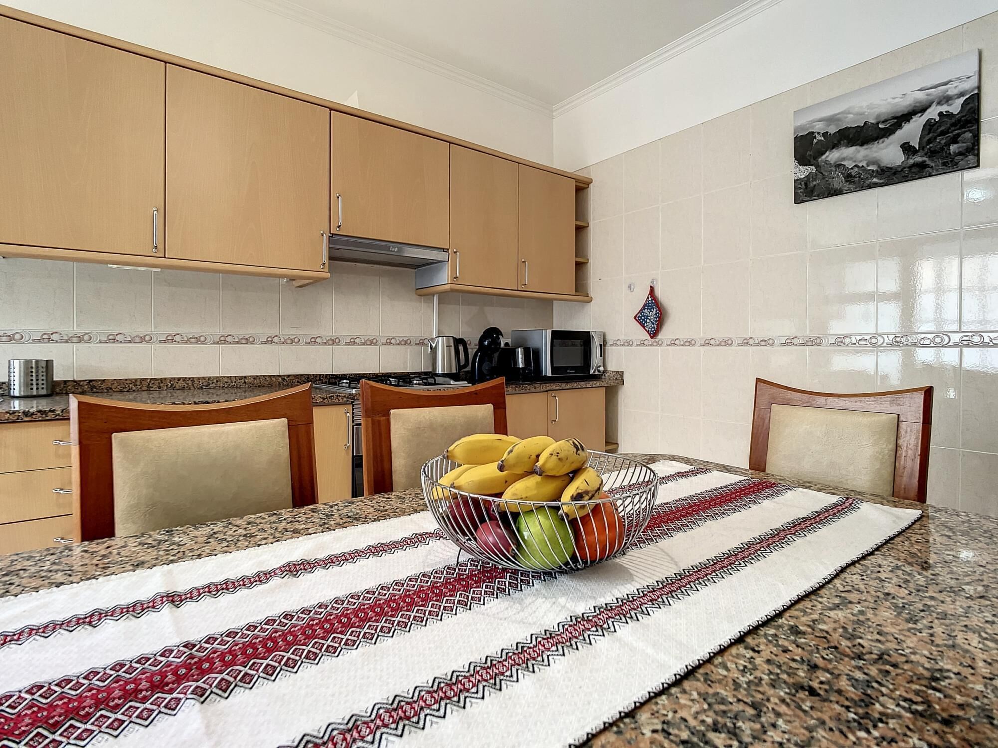Una cocina con armarios de madera, encimera de granito y una mesa de comedor con mantel estampado.