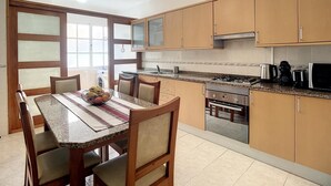A kitchen with wooden cabinets, a gas stove, a microwave, and a dining table with chairs. - Milagres Apartment by Atlantic Holiday (Machico)