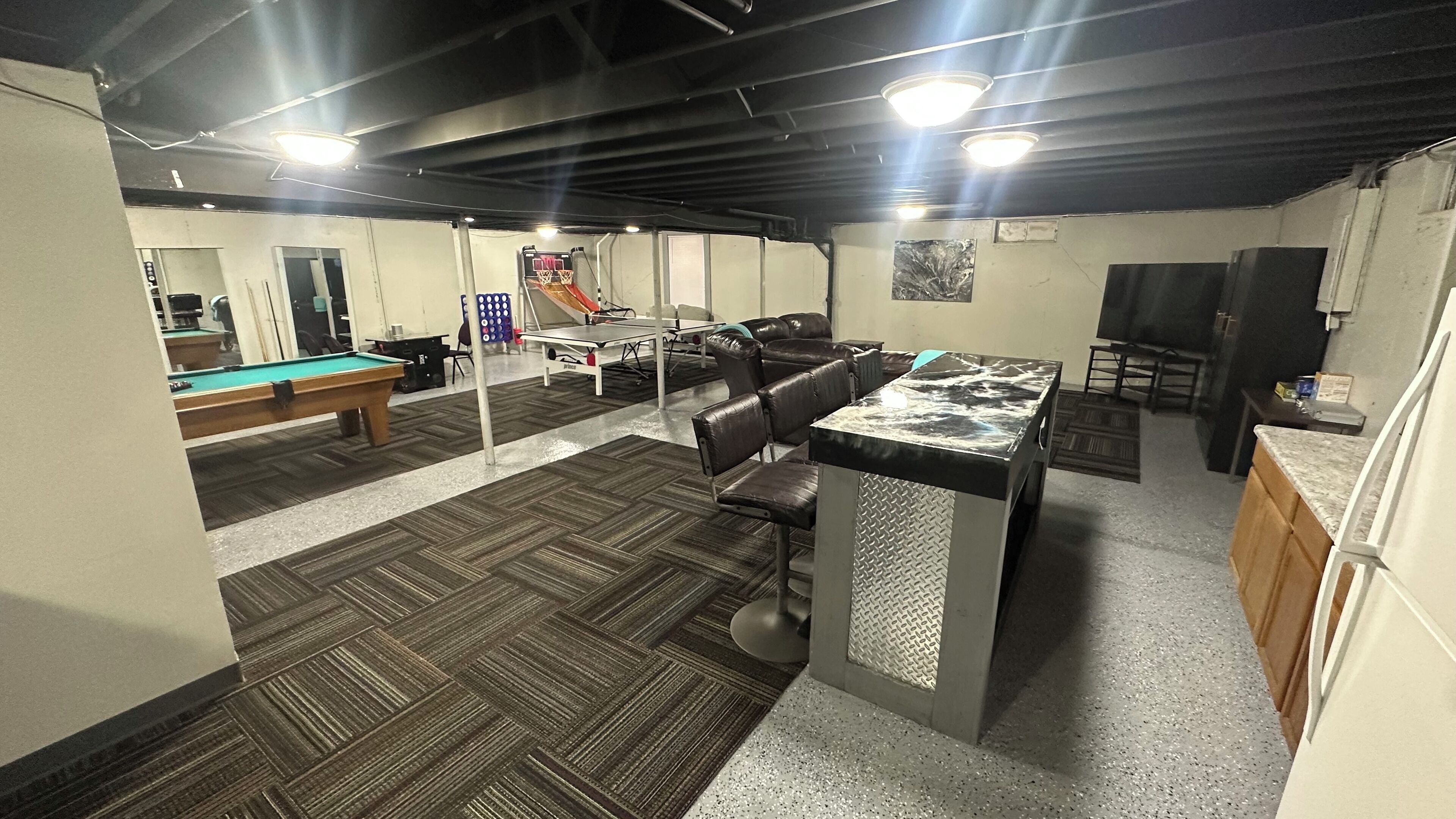 A billiards room with a pool table, chairs, and a bar area.