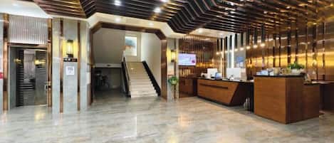 A hotel lobby with a reception desk, a staircase, and a modern ceiling design.