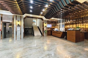 Un vestíbulo de hotel con una recepción, una escalera y un diseño moderno de techo.