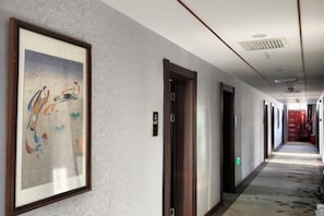 Corredor de hotel com quadros nas paredes, portas e piso coberto por carpete.