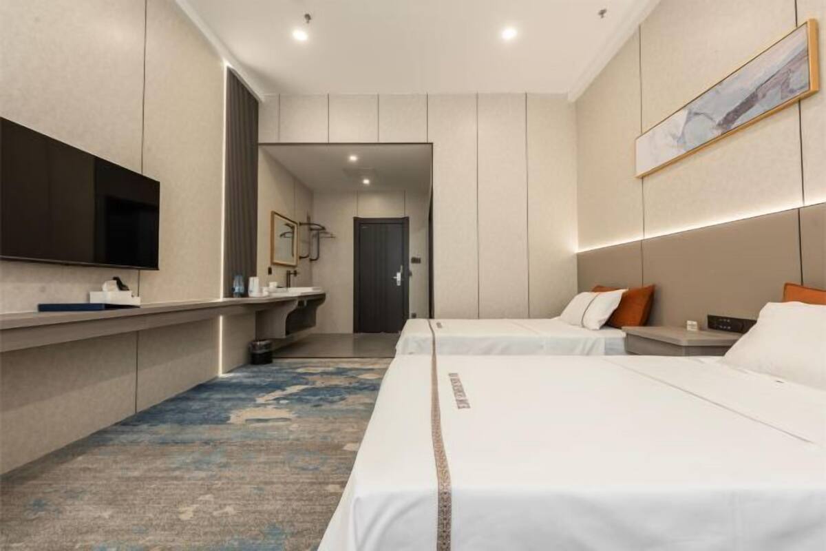 Ein Hotelzimmer mit zwei Betten, einem Fernseher, einem Badezimmer und einem Gemälde an der Wand.