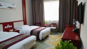 A hotel room with two beds, a desk, a chair, a TV, and a window with curtains.
