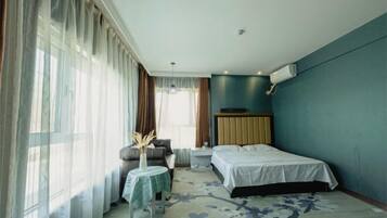 A hotel room with a bed, a small table with a vase, a chair, and a window with curtains.