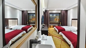 Une chambre d’hôtel avec deux lits, un bureau, un miroir et une vue sur un immeuble par la fenêtre.