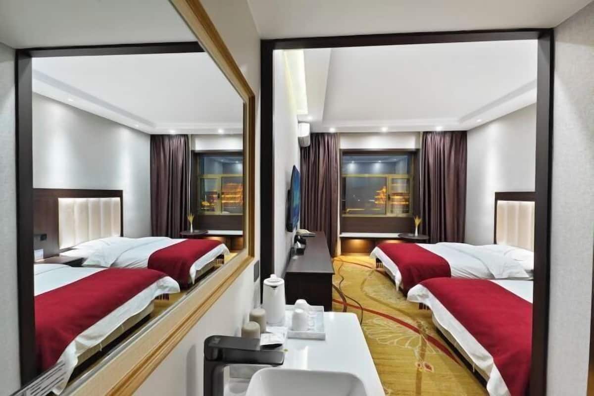 Ein Hotelzimmer mit zwei Betten, einem Schreibtisch, einem Spiegel und Blick auf ein Gebäude durch das Fenster.