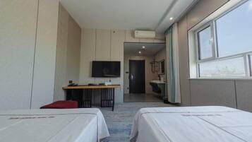 A hotel room with two beds, a desk with a chair, a TV, and a bathroom visible through an open door.