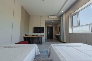 Ein Hotelzimmer mit zwei Betten, einem Schreibtisch mit Stuhl, einem Fernseher und einem durch eine offene Tür einsehbaren Badezimmer.