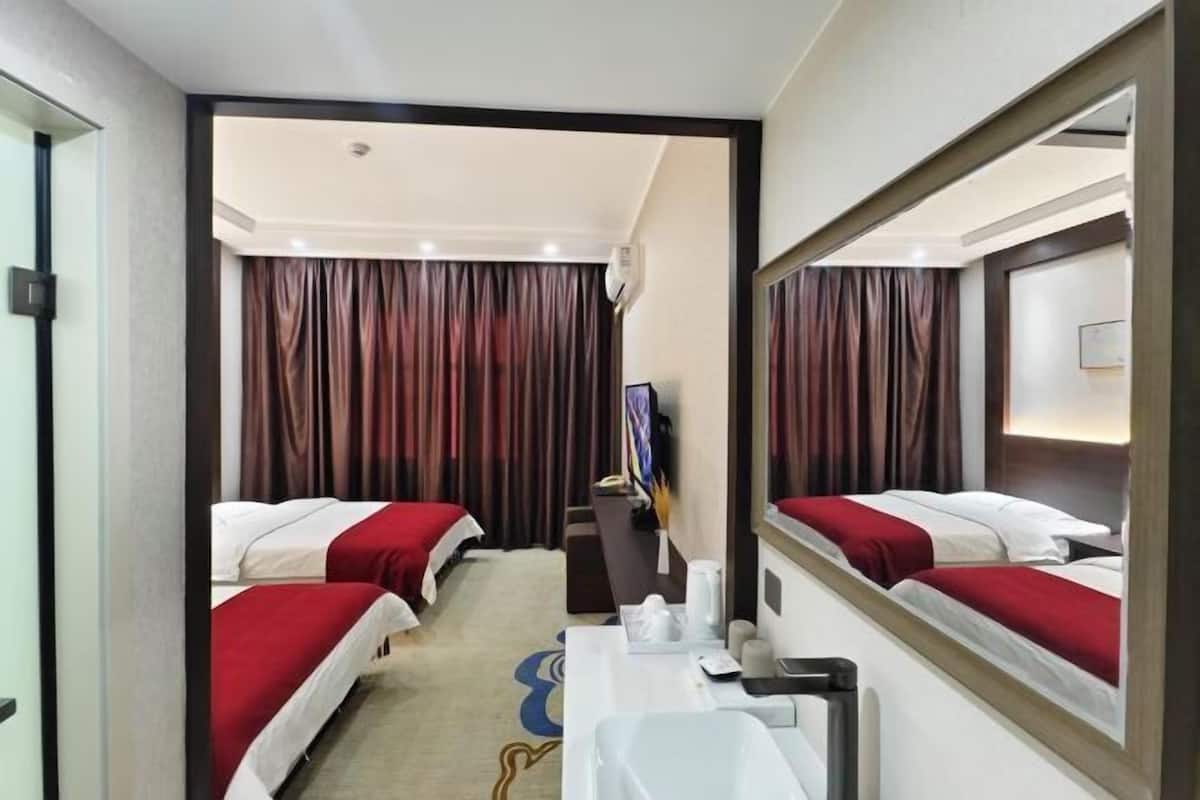 Ein Hotelzimmer mit zwei Betten, einem Schreibtisch, einem Spiegel und Blick auf den Flur.