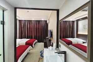 Une chambre d’hôtel avec deux lits, un bureau, un miroir et une vue sur le couloir.