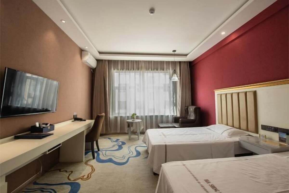 Ein Hotelzimmer mit Bett, Schreibtisch, Stuhl, Fernseher und einem Fenster mit Vorhängen.