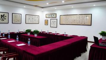 A conference room with long tables, chairs, and framed calligraphy on the walls.